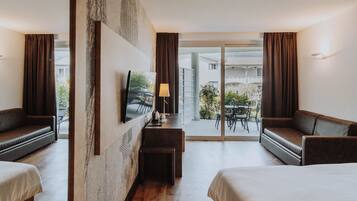 A hotel room with two beds, a desk, a TV, and a balcony with a table and chairs.