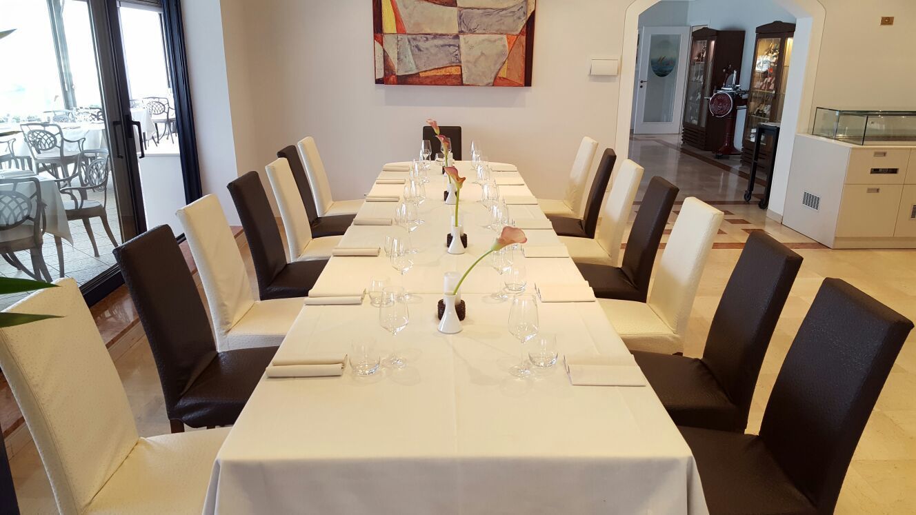 Una larga mesa de comedor con manteles blancos, sillas negras y cristalería transparente.
