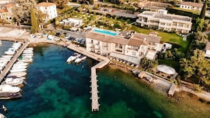 Vista aérea de un hotel costero con un puerto deportivo, una piscina y un jardín.
