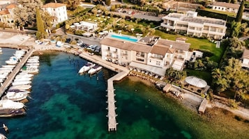 Vista aérea de un hotel costero con un puerto deportivo, una piscina y un jardín.