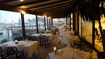 Un restaurant avec des tables dressées, offrant une vue sur un port de plaisance.
