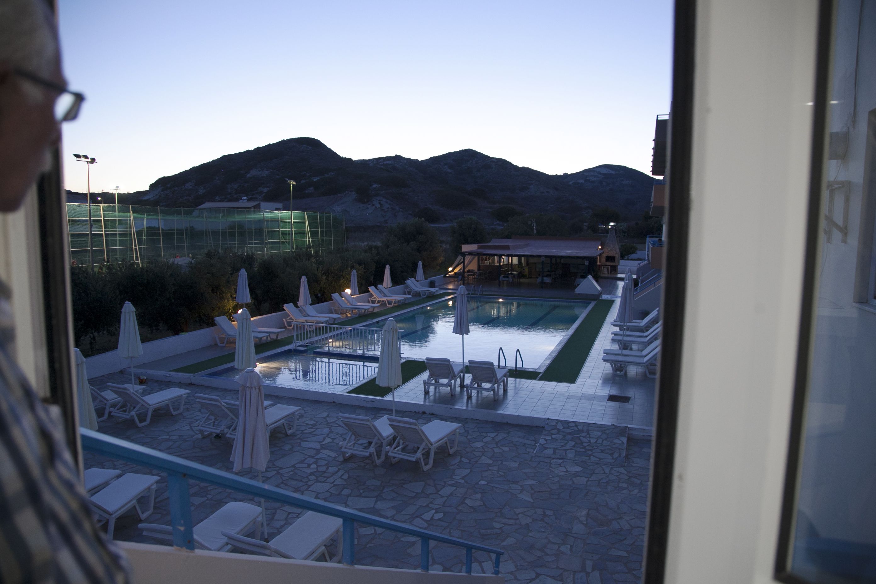 A pool area with lounge chairs and umbrellas, a covered seating area, and a view of mountains in the background.