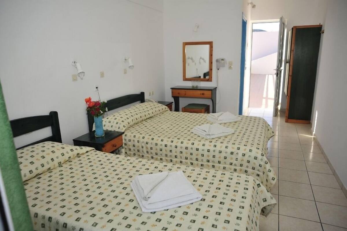A hotel room with two beds, a nightstand, a dresser, a mirror, and a door leading to another room.