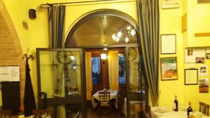 An interior view of a restaurant with tables set for dining, a visible menu board, and a brick wall. - Oasi del grillo (Castelnuovo Berardenga)