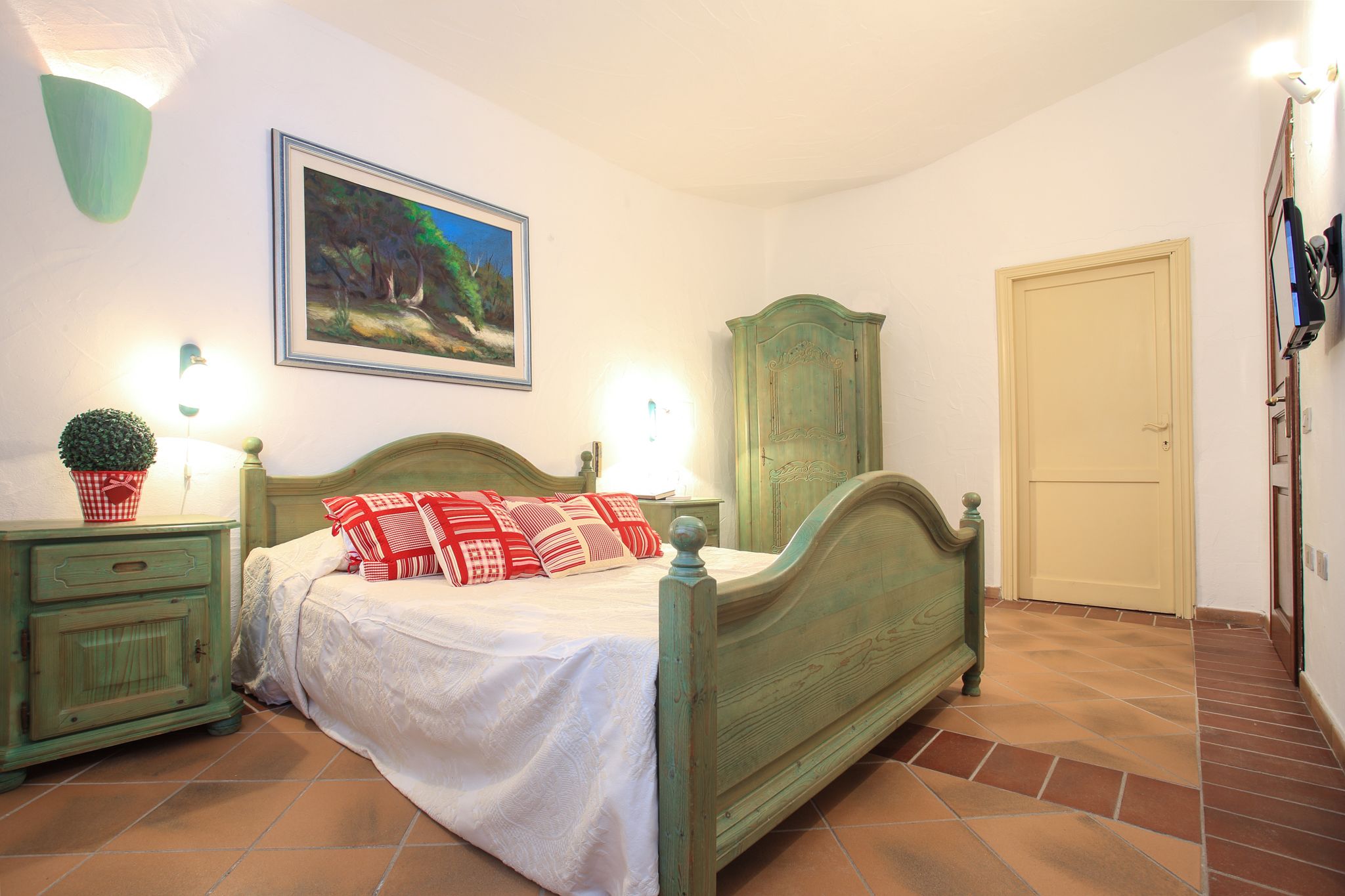 A bedroom with a bed, a nightstand, a cabinet, a door, and a wall-mounted picture.