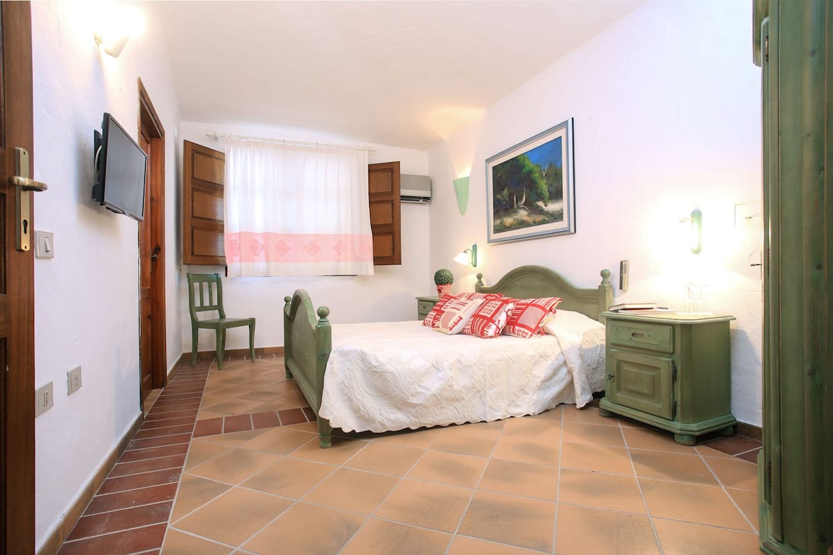 A bedroom with a bed, a chair, a nightstand, and a television.