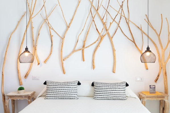 A bedroom with a bed, two bedside tables, a wall-mounted lamp, and a wall decor of branches.