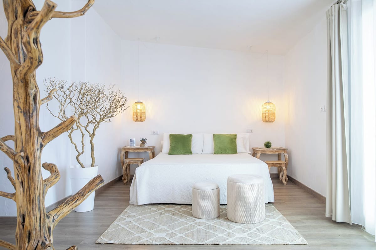 A bedroom with a large bed, two bedside tables, a nightstand, a potted plant, and a decorative tree trunk.