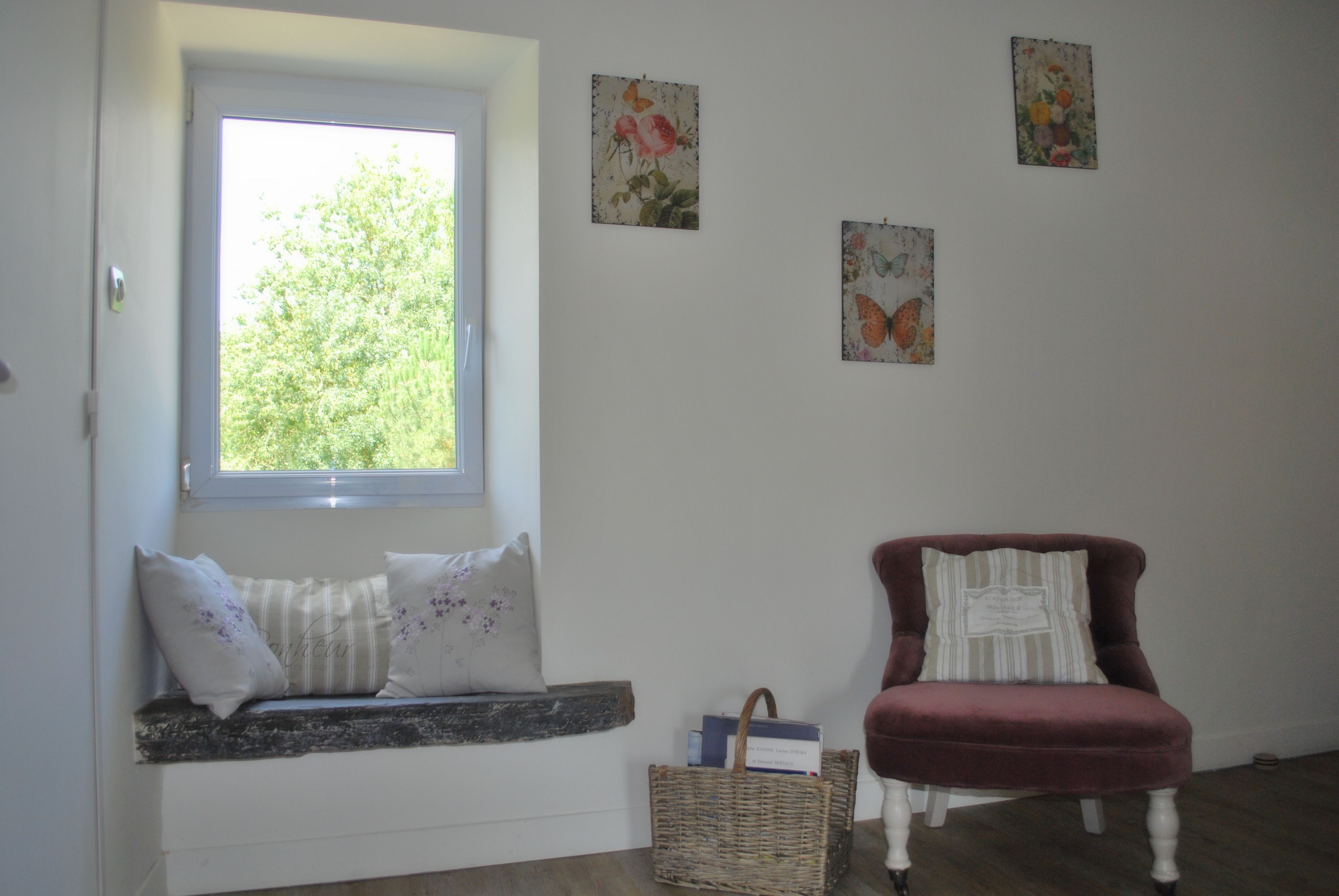 A room with a window seat, a red armchair, and wall art.