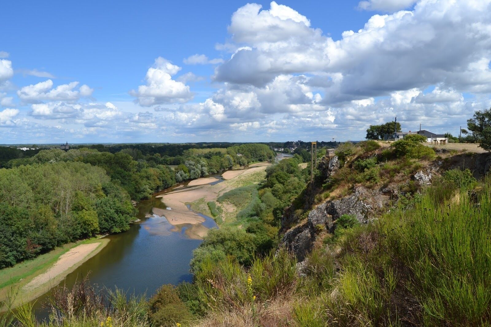 A river flowing through a valley with a castle in the distance, surrounded by dense forests and a clear sky.