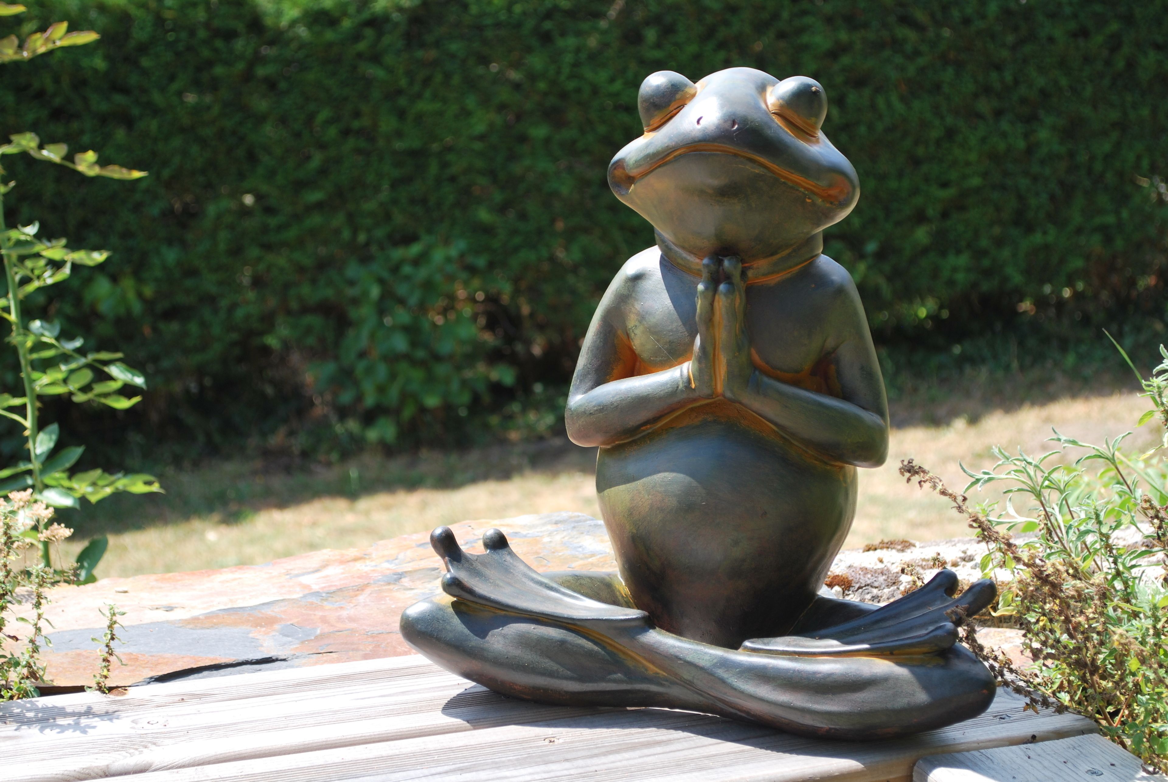 A frog statue in a meditative pose on a wooden platform.