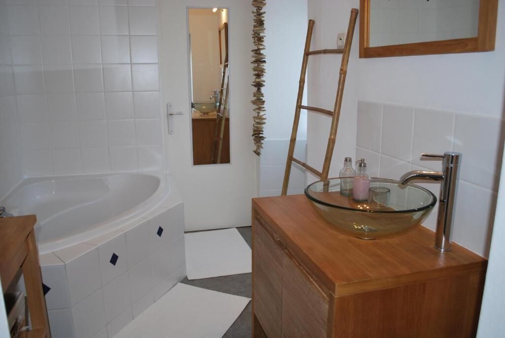 Un baño con una bañera blanca, un tocador de madera con un lavabo de vidrio y un espejo sobre el lavabo.
