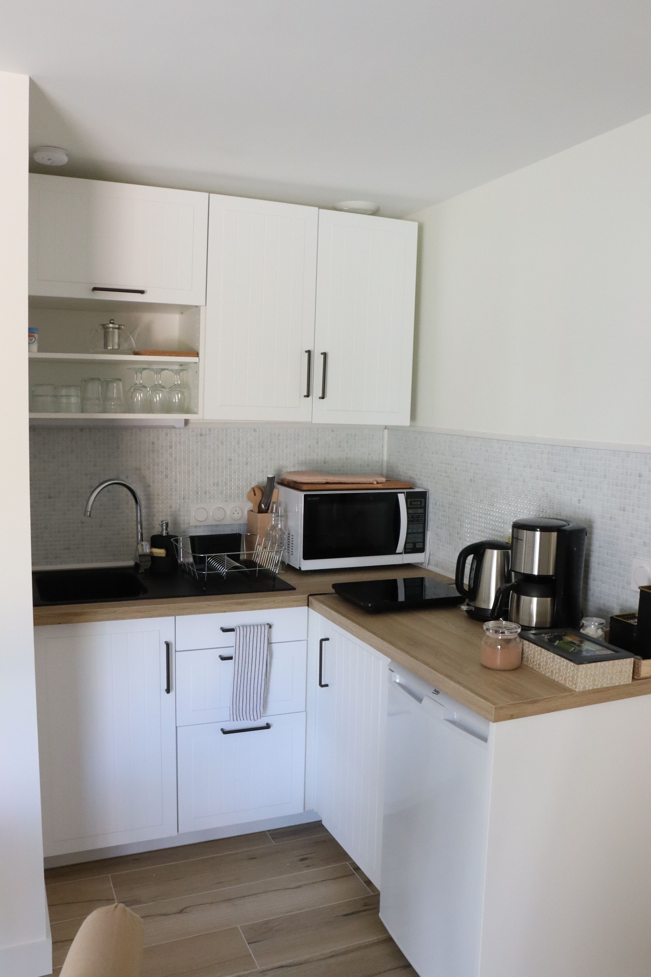 A compact kitchen with white cabinets, a microwave, a coffee maker, and a sink.