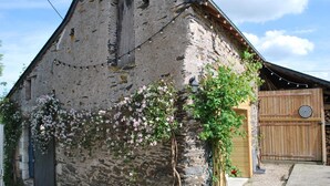 A rustic stone building with a wooden door and a small garden area with flowering plants. - La Petite Boire - chambres d'hôtes (Murs-Erigne)