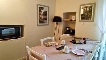 Un coin repas avec une table dressée pour quatre personnes, des chaises blanches, une lampe et des tableaux encadrés accrochés aux murs.