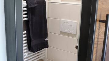 A compact bathroom with a white toilet, a towel rack, a mirror, and a towel hanging on the rack.