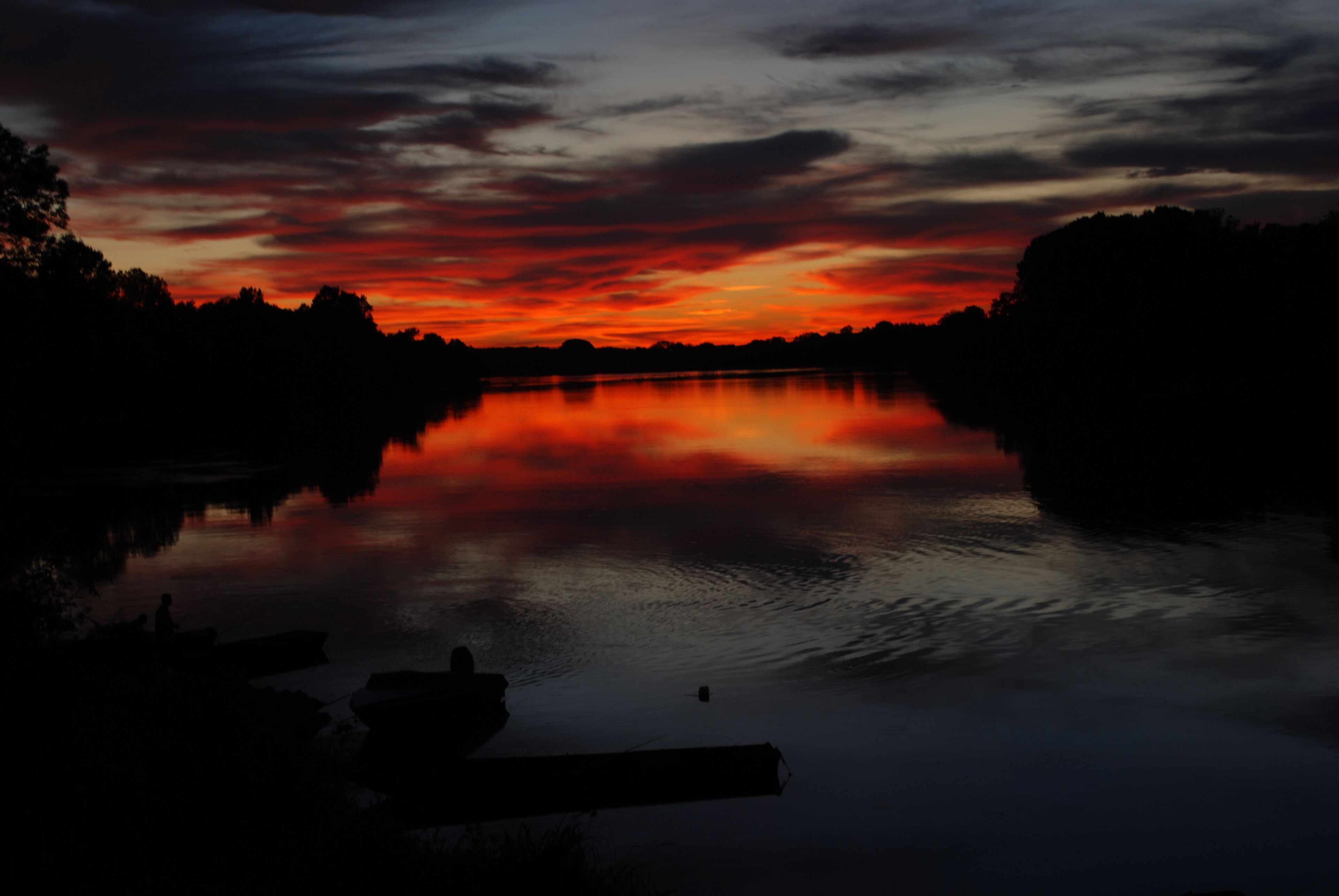 Una puesta de sol serena sobre un río tranquilo con barcos amarrados a la izquierda.