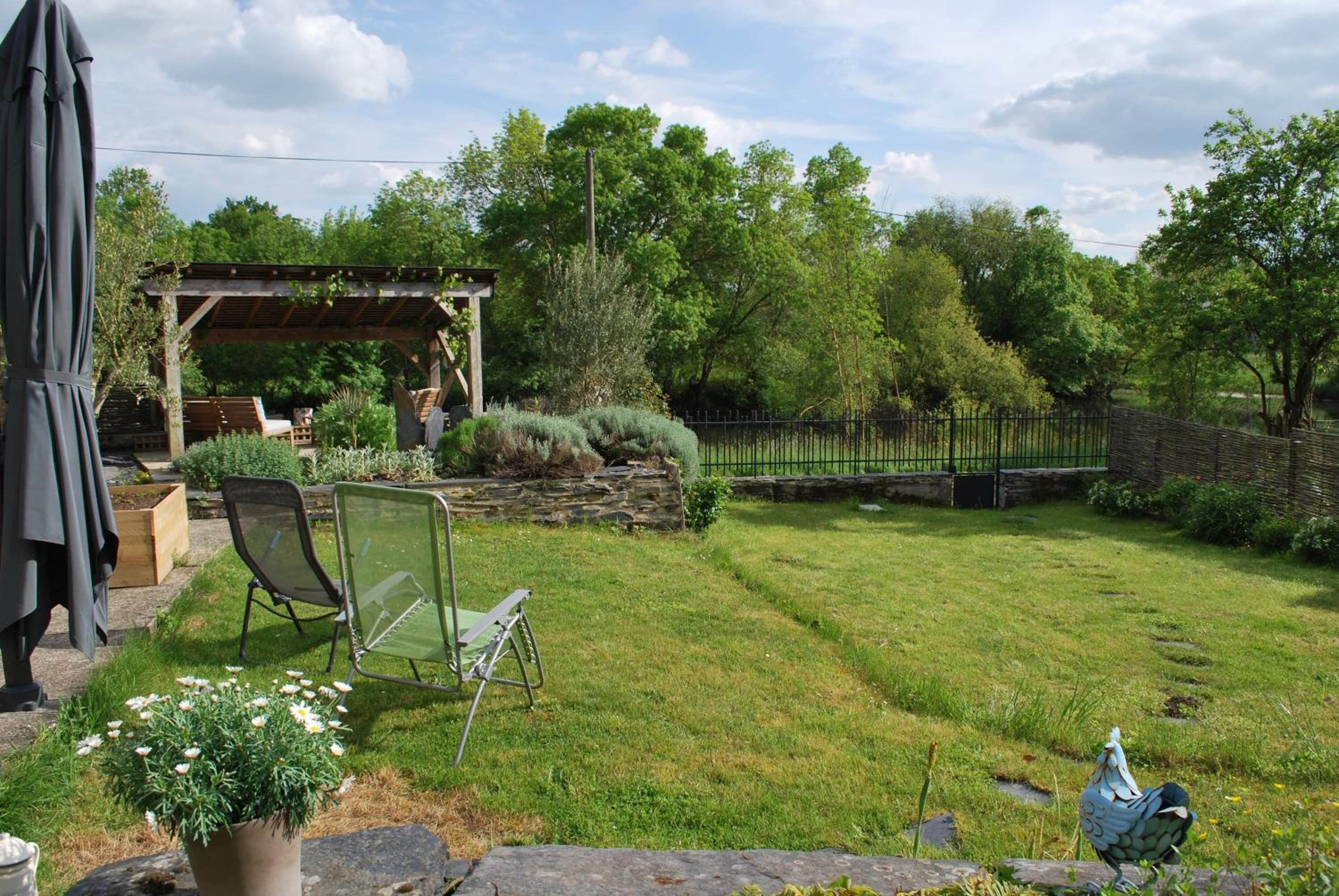 A backyard with a pergola, a lawn, a stone wall, and a fence.