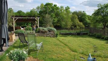 A backyard with a pergola, a lawn, a stone wall, and a fence.