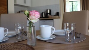 A dining table with a vase of flowers, white cups, and a glass of water. - La Petite Boire - chambres d'hôtes (Murs-Erigne)