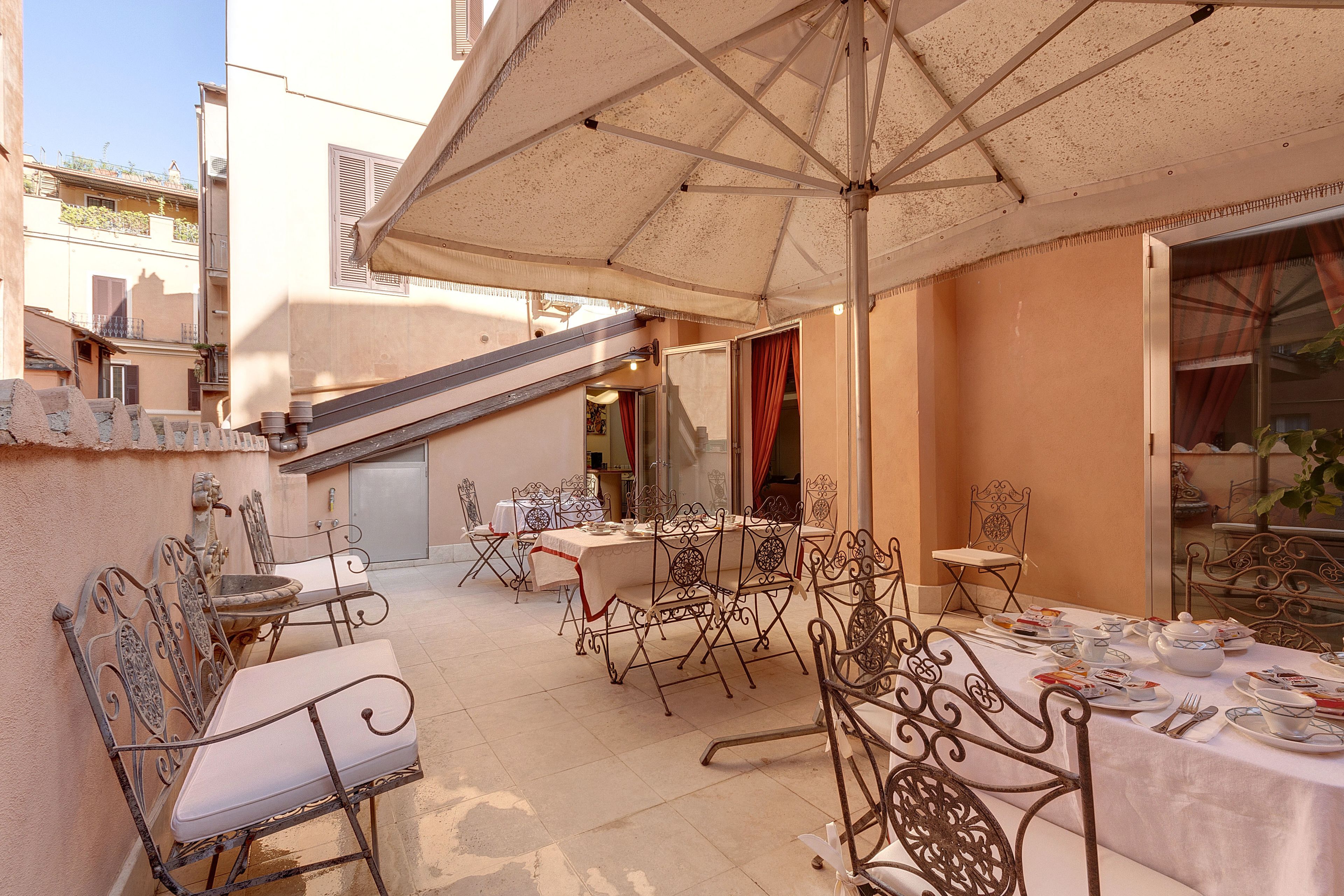 An outdoor dining area with metal chairs and tables, covered by a large umbrella.