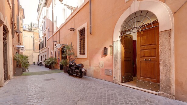 A narrow cobblestone street with a parked scooter, a wooden door, and a small potted plant. - LM Suite Spagna (Rome)