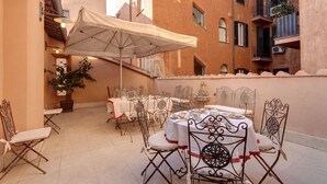 An outdoor dining area with tables and chairs, a large umbrella, and potted plants. - LM Suite Spagna (Rome)