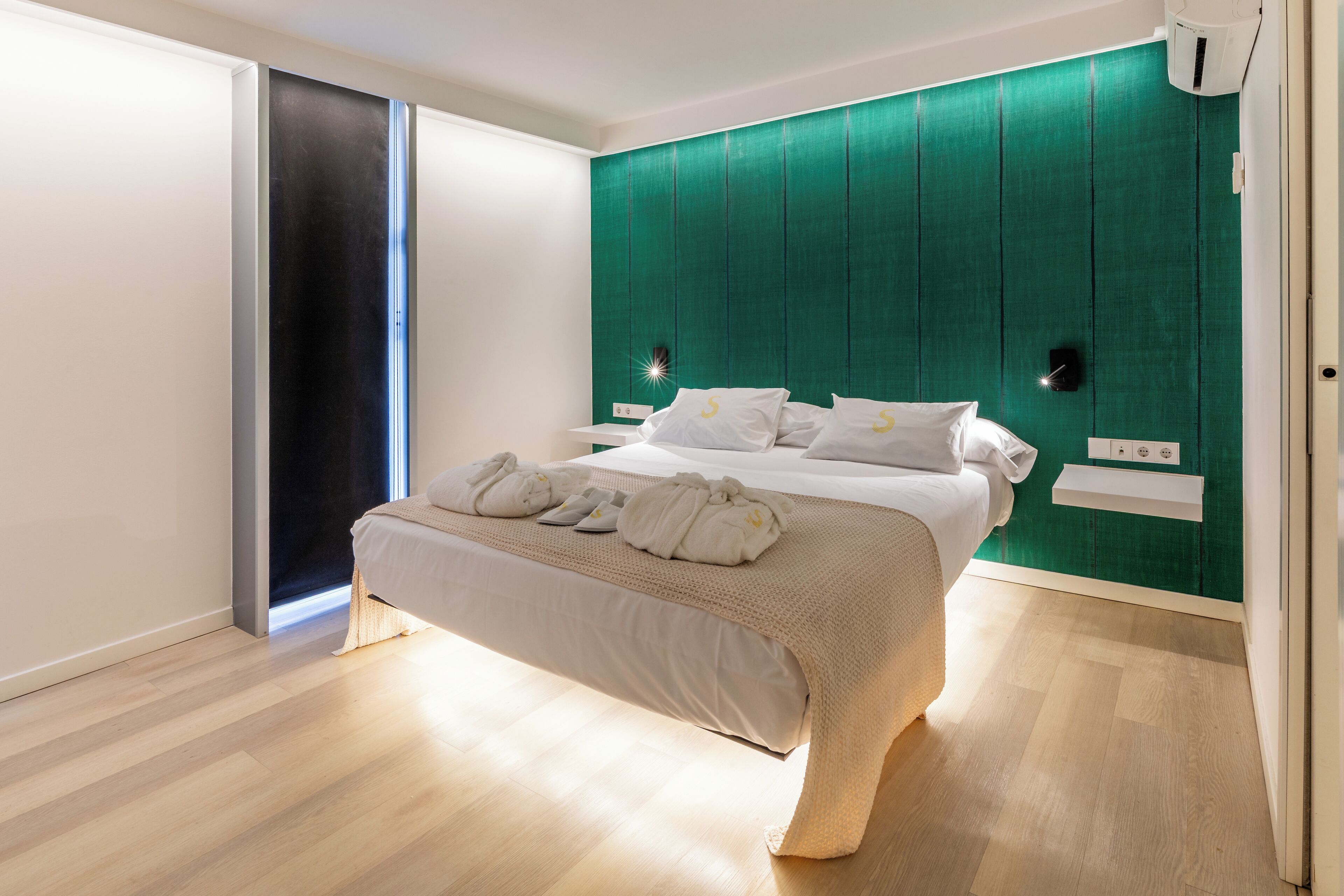Un dormitorio moderno con cama, pared de acento verde, suelo de madera y puerta corrediza.