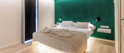 A modern bedroom with a bed, a green accent wall, a wooden floor, and a sliding door.