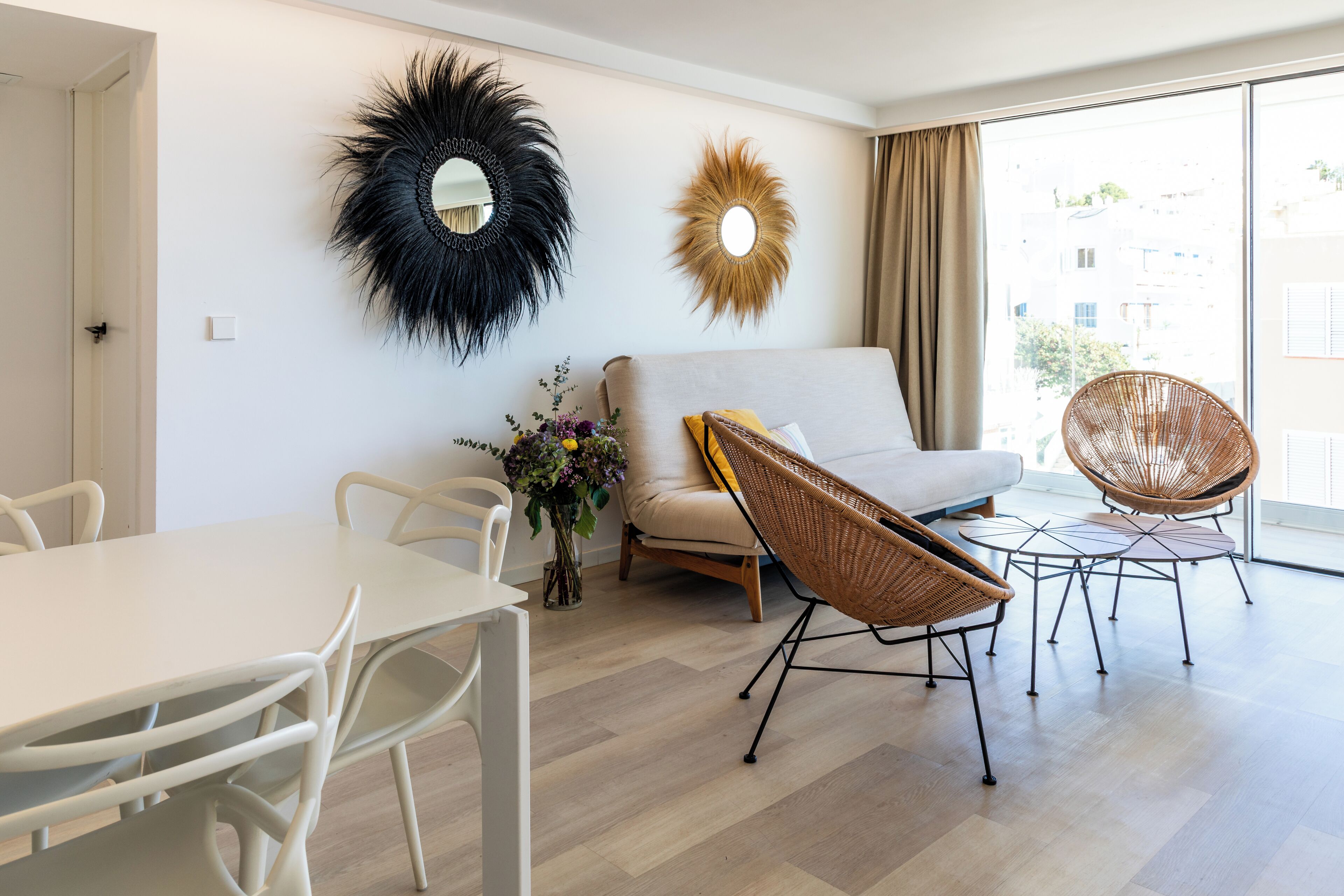 Una sala moderna con sofá, dos sillones de mimbre, una mesa de comedor y decoración en la pared.