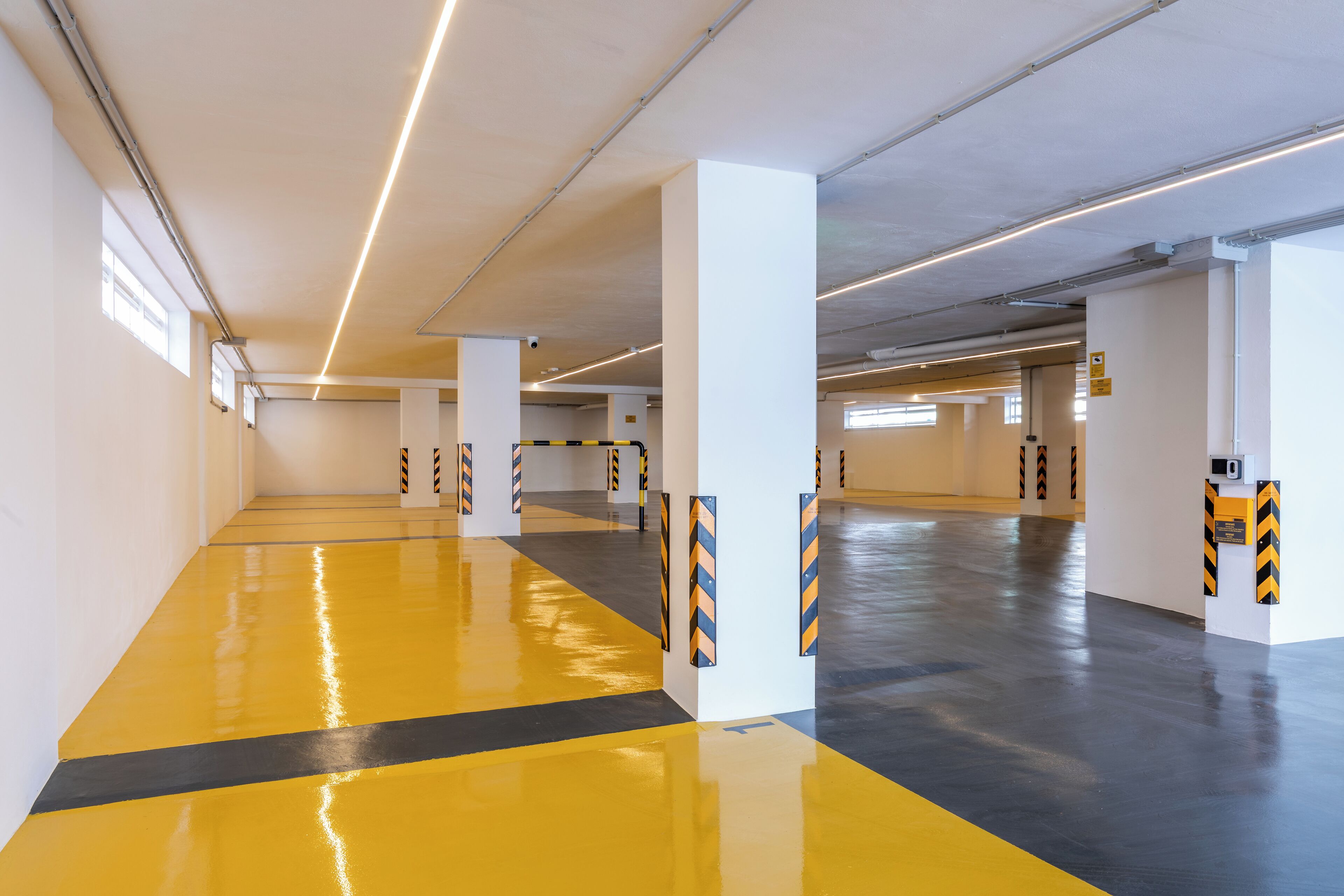 Een ruime parkeergarage met gele en zwarte strepen, witte pilaren en verlichting aan het plafond.