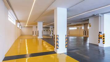 Een ruime parkeergarage met gele en zwarte strepen, witte pilaren en verlichting aan het plafond.