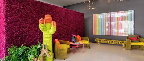 Un interior moderno con una pared roja vibrante, una escultura de cactus, muebles de mimbre y un cuadro abstracto y colorido.