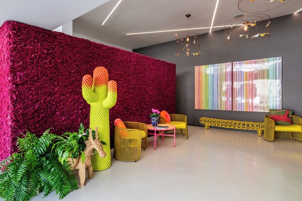 Un interior moderno con una pared roja vibrante, una escultura de cactus, muebles de mimbre y un cuadro abstracto y colorido.