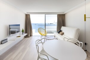 Una sala de estar moderna con un ventanal grande, un televisor de pantalla plana, un sofá blanco, una mesa de comedor y una silla amarilla.