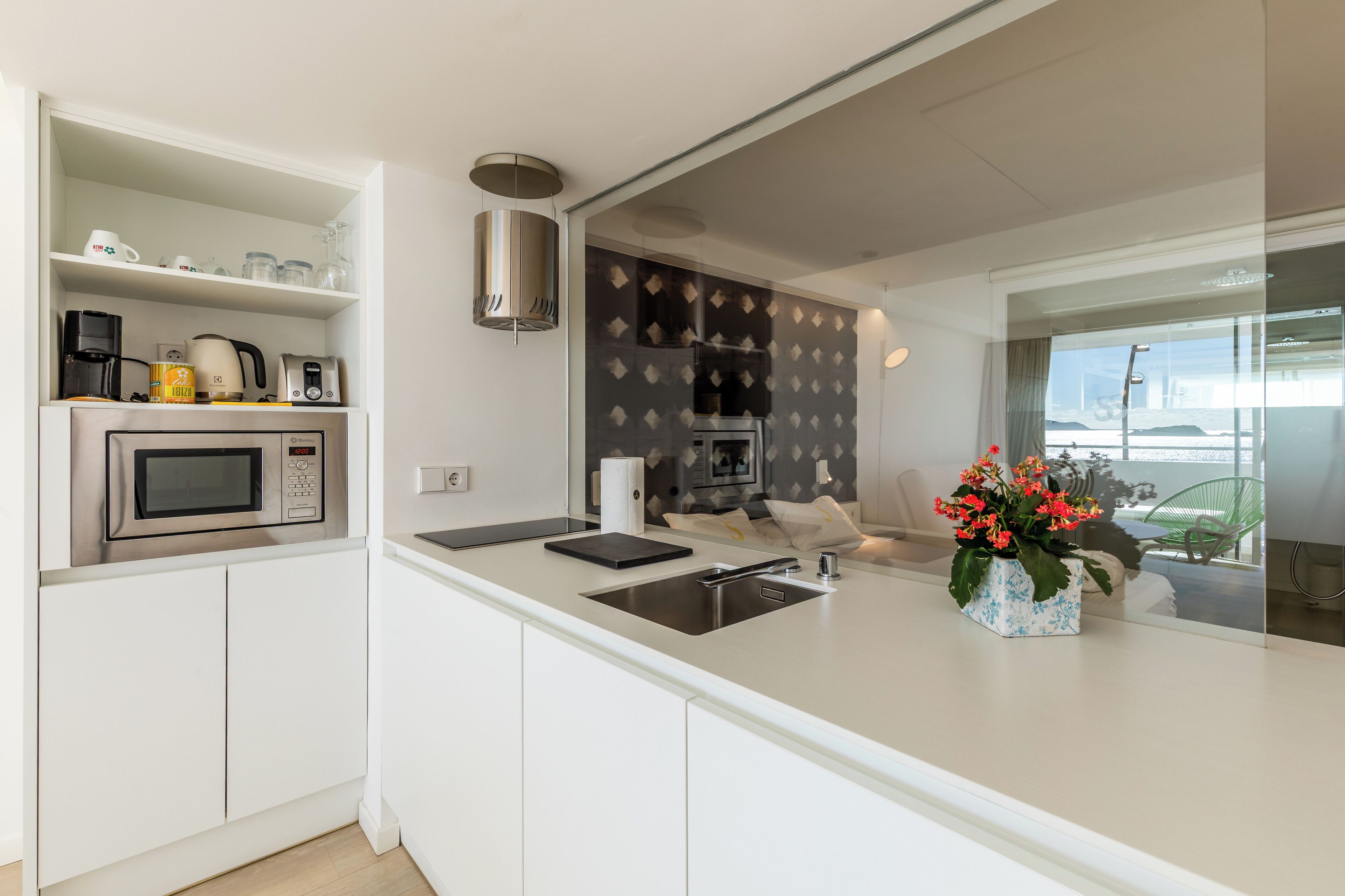Una cocina moderna con armarios blancos, un lavaplatos de acero inoxidable, microondas, cafetera y una planta decorativa.