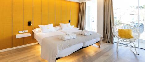 A modern hotel room with a large bed, a bright yellow wall, and a view of the city through large windows.
