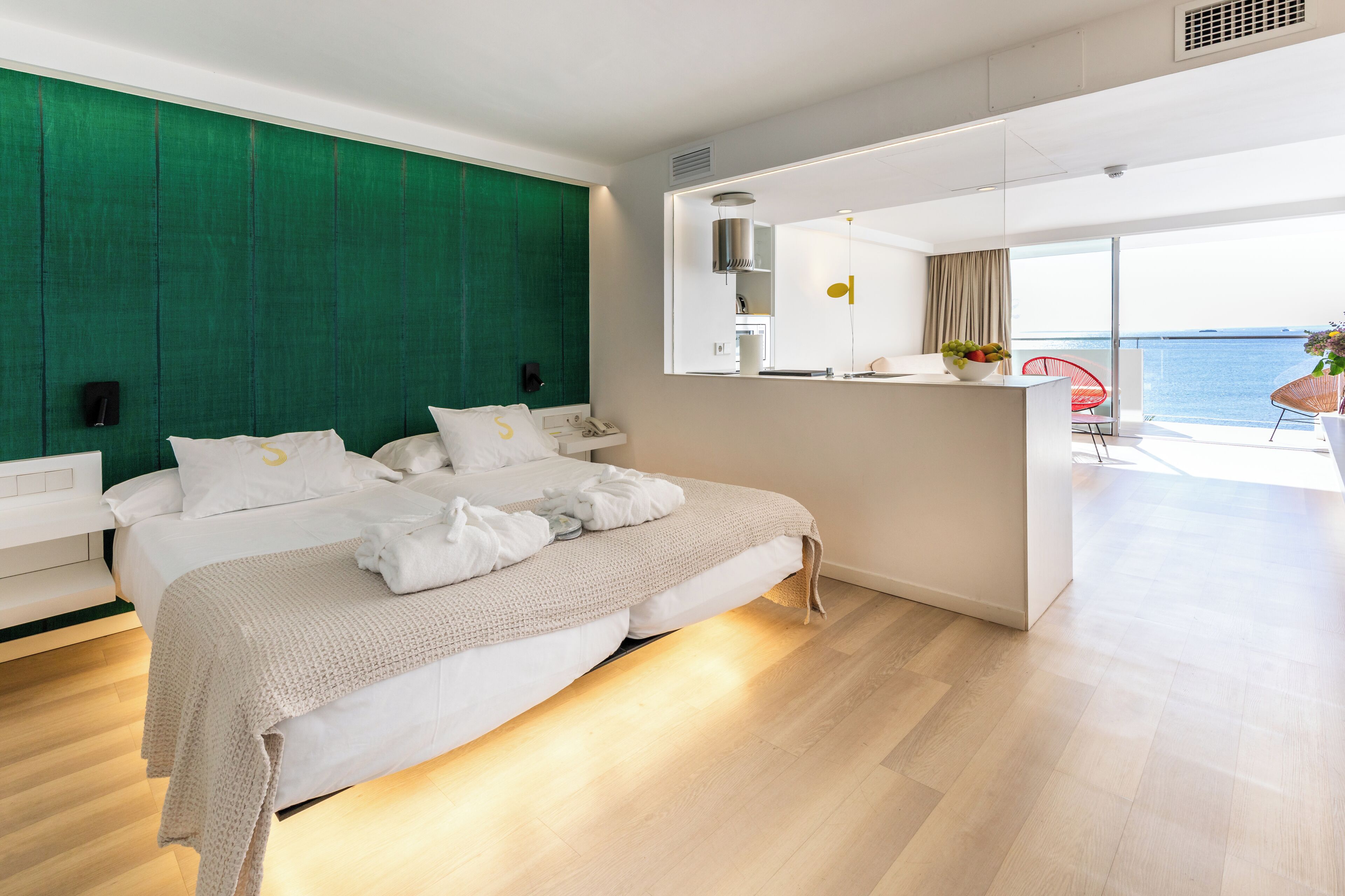 Habitació d'hotel moderna amb un llit gran, una paret d'accent verd, una zona de cuina i un balcó amb vista al mar.