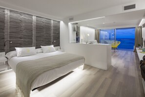 Una habitación de hotel moderna con una cama grande, un balcón con vistas al océano y un diseño minimalista.