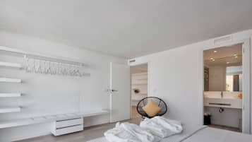 Een moderne slaapkamer met een bed, nachtkastje, fauteuil en inloopkast.