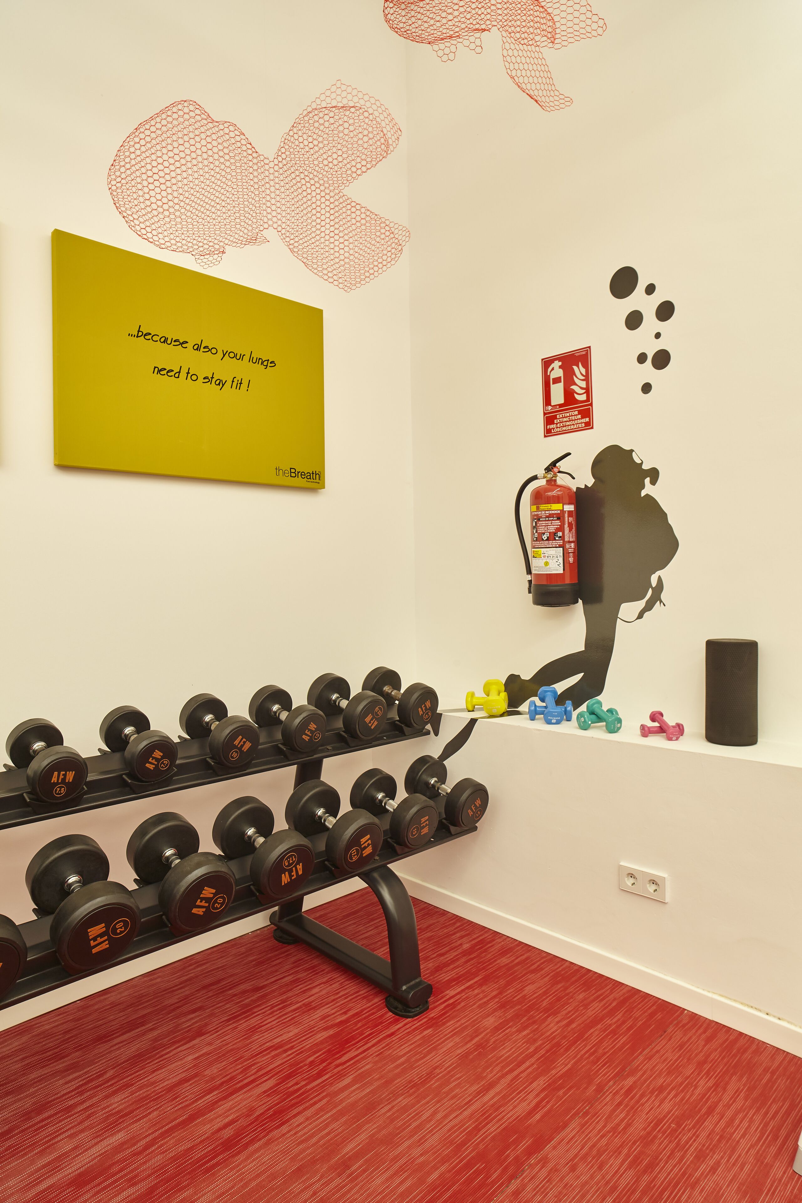 A gym with dumbbells, a fire extinguisher, and a motivational quote on the wall.