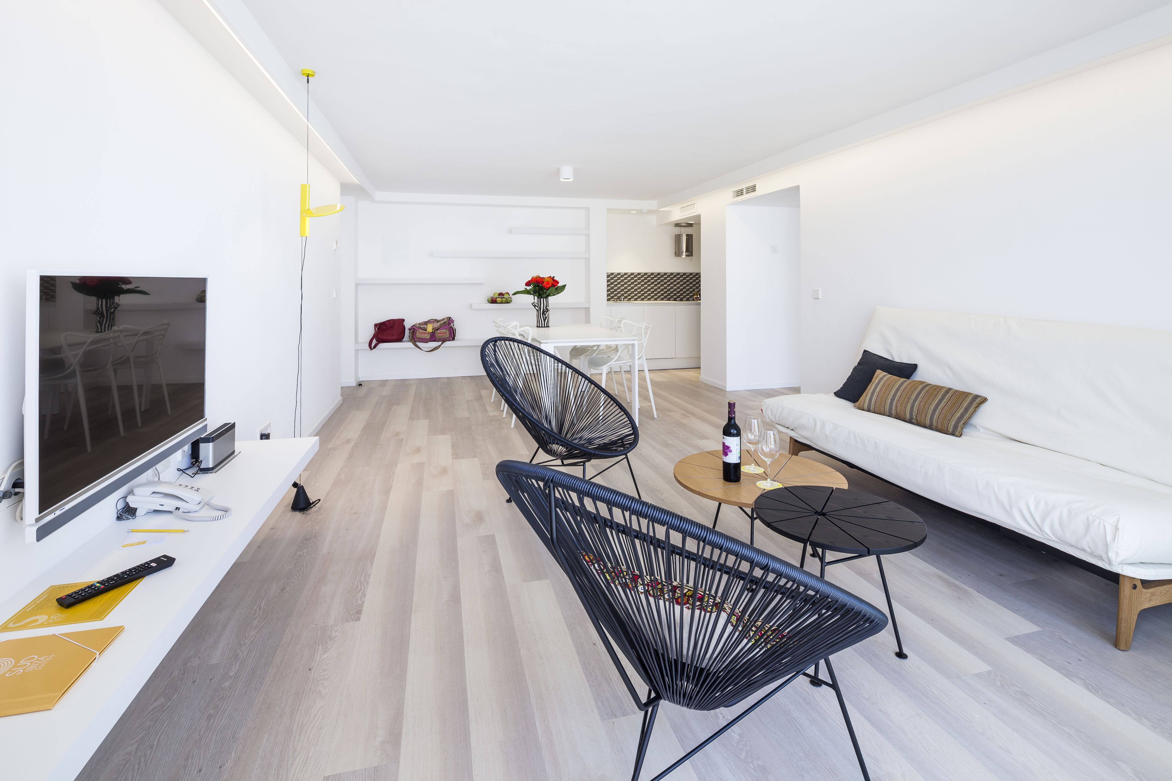 Una sala de estar moderna con un televisor de pantalla plana, un sofá, un comedor con sillas y una pequeña cocina al fondo.