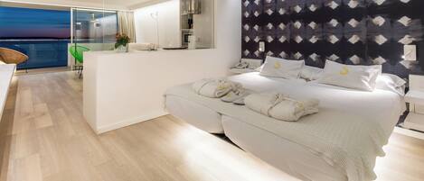 A modern hotel room with a large bed, a balcony with a view, a small kitchenette, and a large mirror.