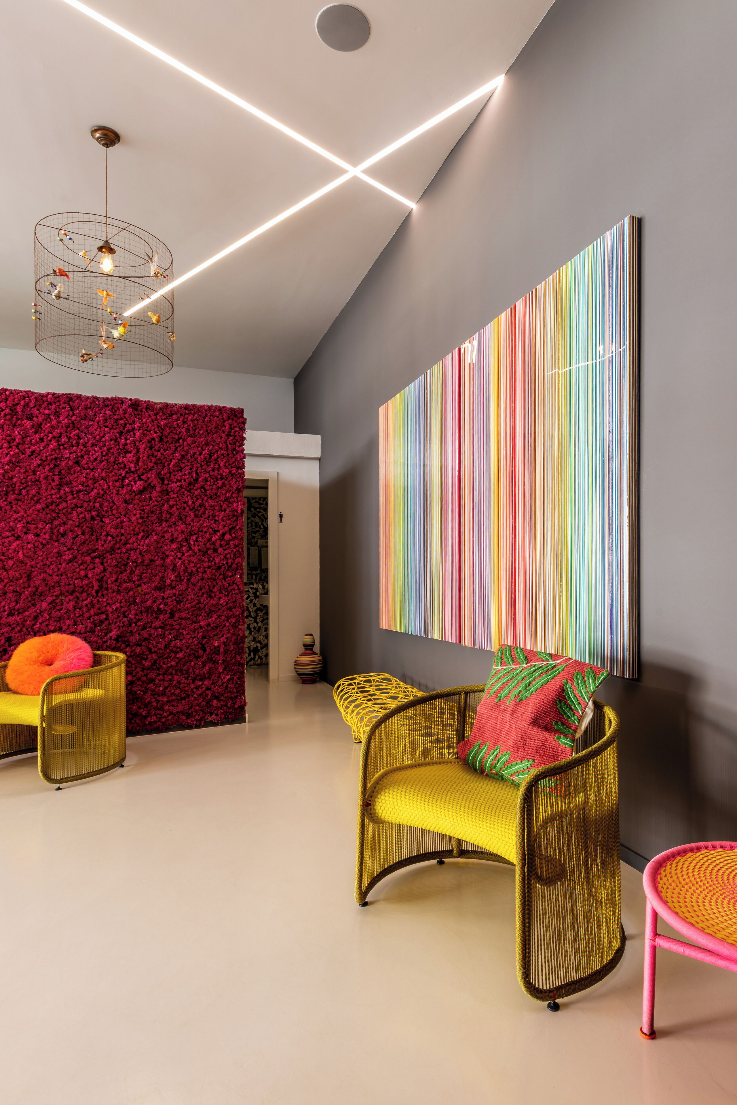 A modern interior with a red textured wall, a large colorful striped artwork, and a yellow wicker chair with a red pillow.
