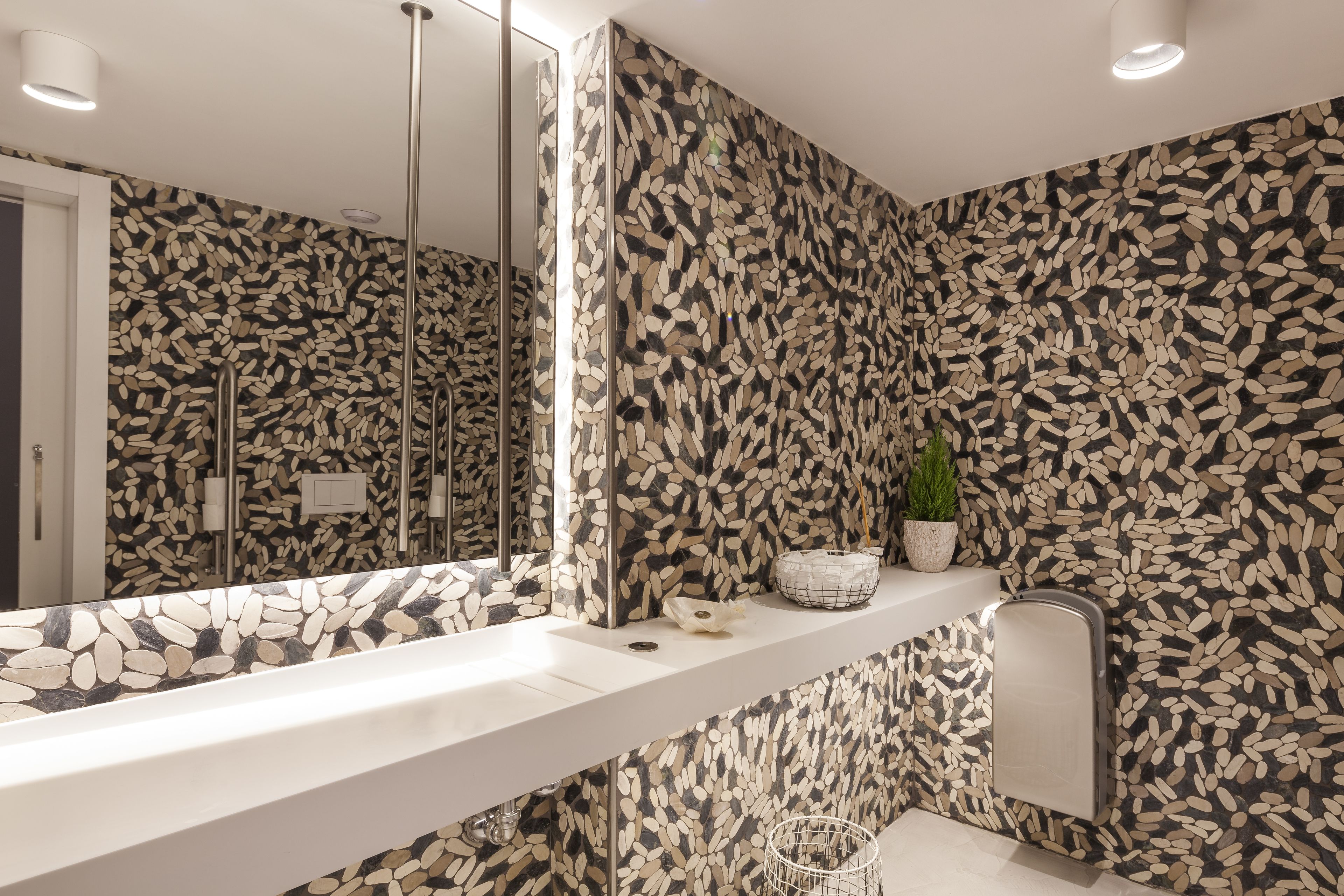 A bathroom with a white sink, a mirror, a towel rack, and a patterned wall.