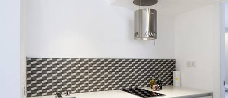 Eine moderne Küche mit weißer Arbeitsplatte, einem Edelstahl-Spülbecken, einer schwarz-weißen Spritzschutzwand und einer zylindrischen Deckenleuchte.