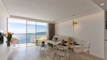 Una sala de estar moderna con un balcón con vistas al mar, un comedor con muebles blancos y una decoración minimalista.