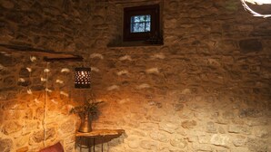 A stone-walled room with a small window, a hanging light fixture, and a table with a potted plant.
