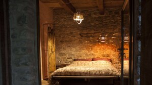 A bedroom with a stone wall, a wooden bed, and a hanging light fixture.