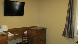 A hotel room with a bed, a desk, a chair, a television, and a window with curtains. - Reynolds Hotel (Lillooet)